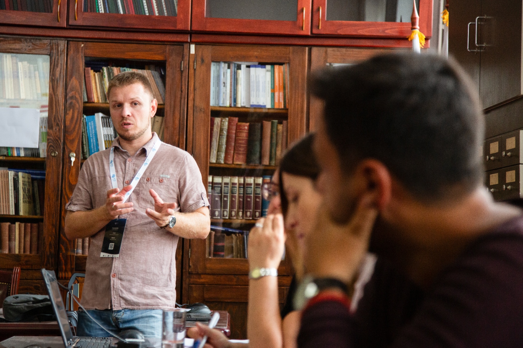 Instructor gesturing to a small group during a hospitality training session in a book-lined room